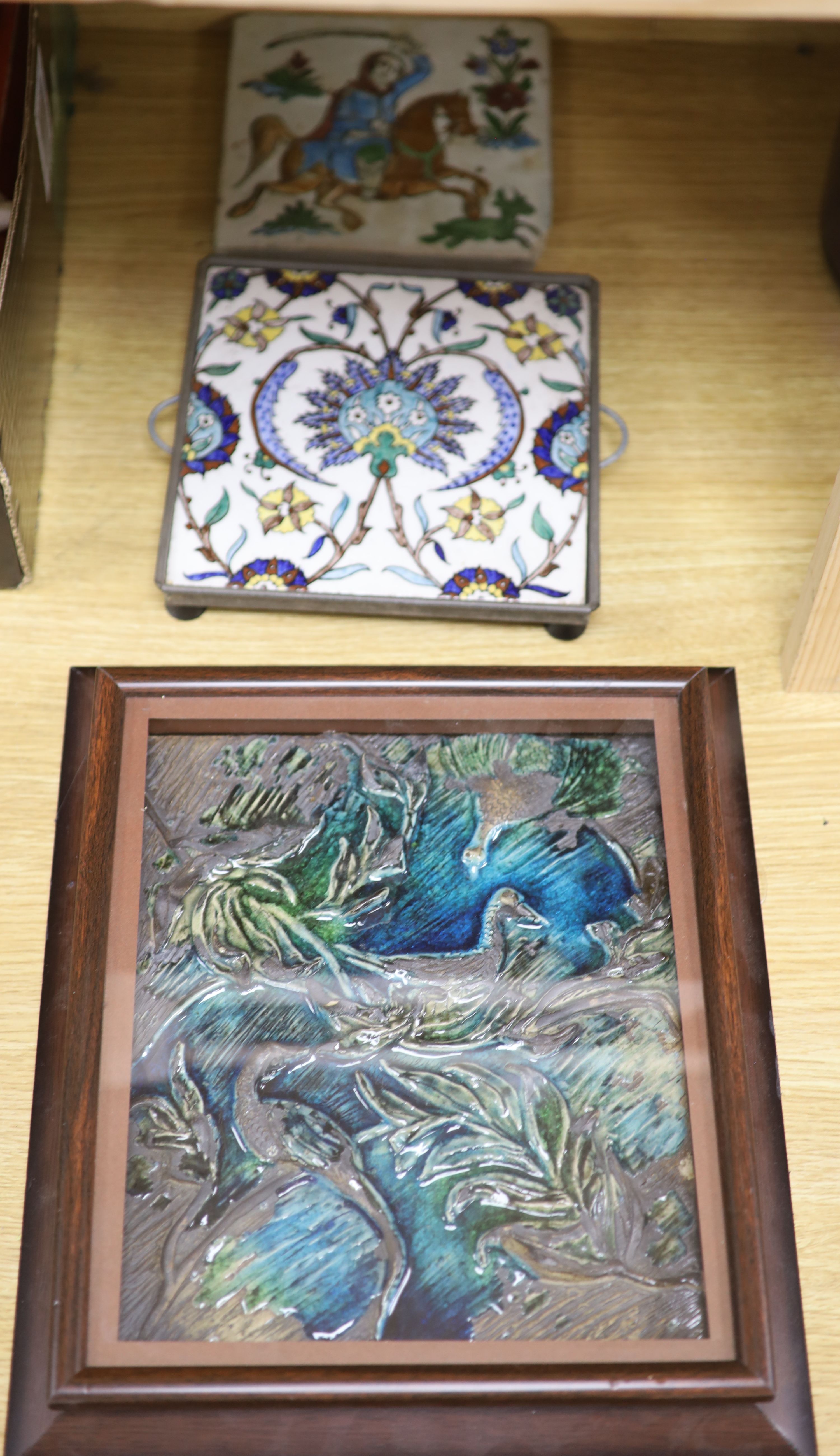 A framed glazed earthenware plaque, a tin glazed tile and one other